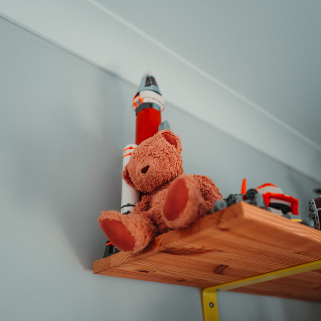 A teddy bear sits on a shelf in a child's room