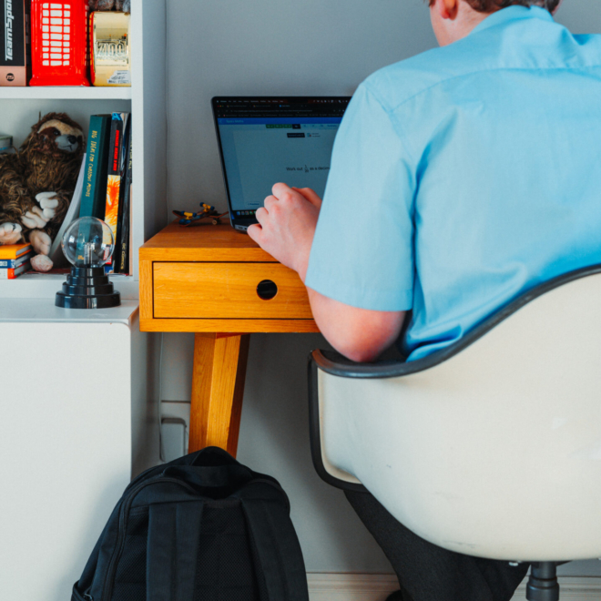 A teenage boy working on his computer in his room
